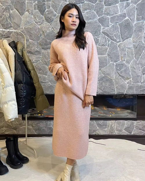 Woman in a pink dress standing in front of a stone wall with clothing racks.