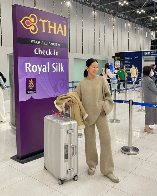 woman with a suitcase at a Thai Airways check-in counter in an airport.