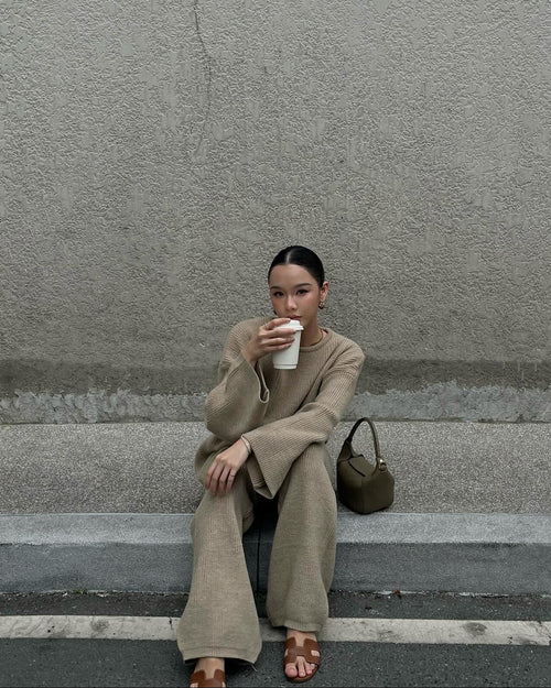 woman sitting on steps drinking from a cup against a gray wall