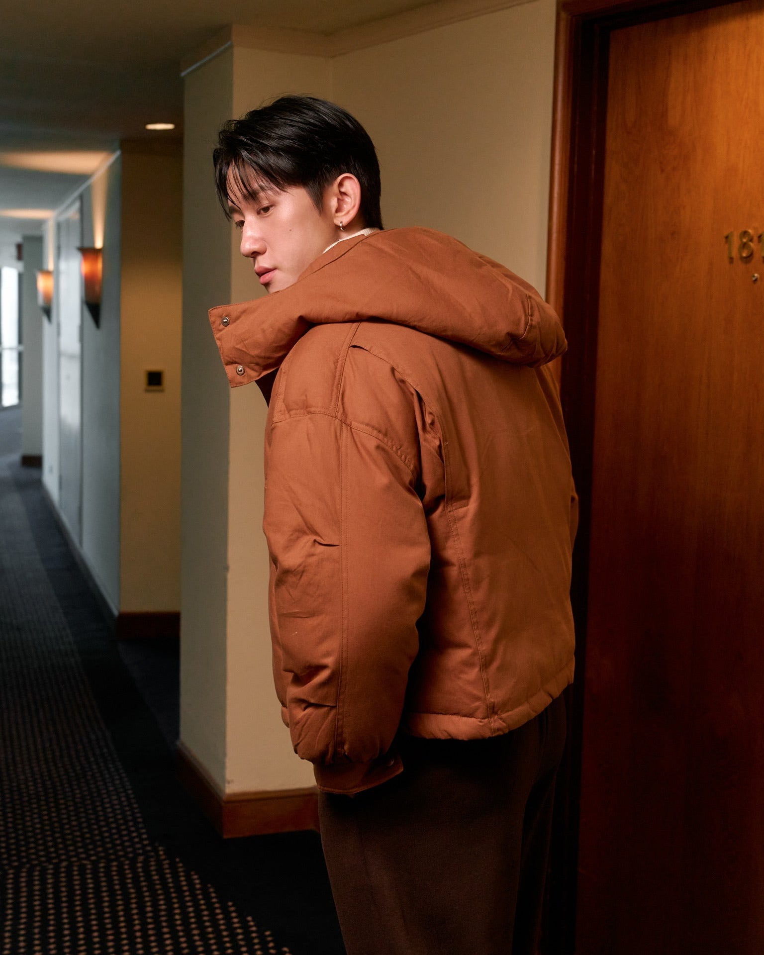 man wearing a brown jacket standing in a hallway
