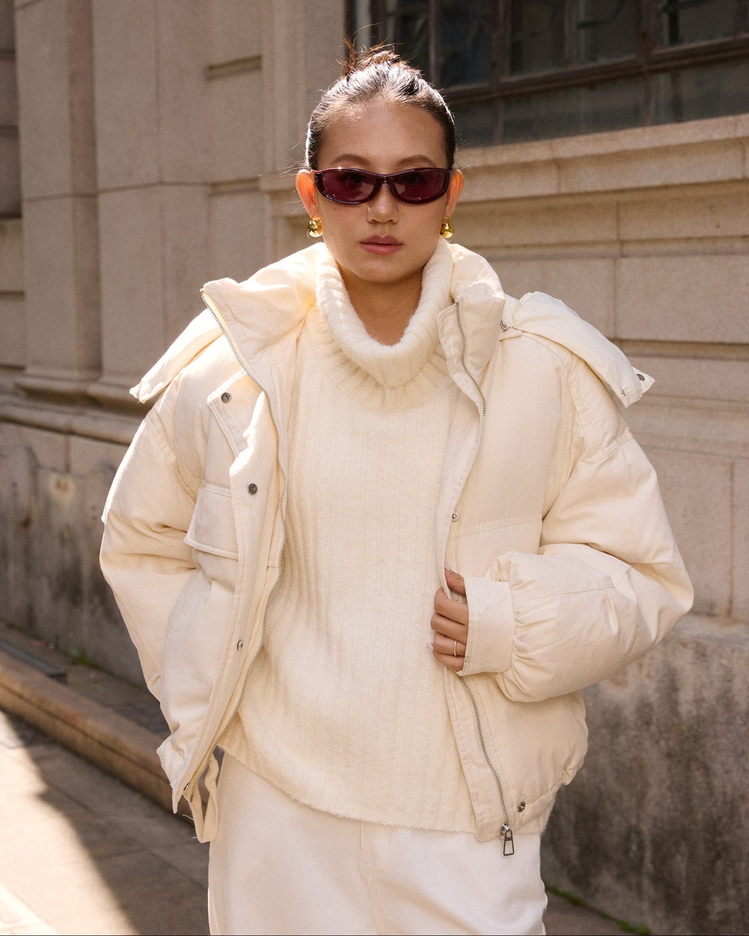 woman wearing a cream-colored puffer jacket and sunglasses outdoors.