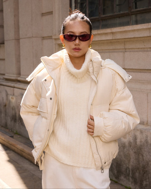 woman wearing a cream-colored puffer jacket and sunglasses outdoors.
