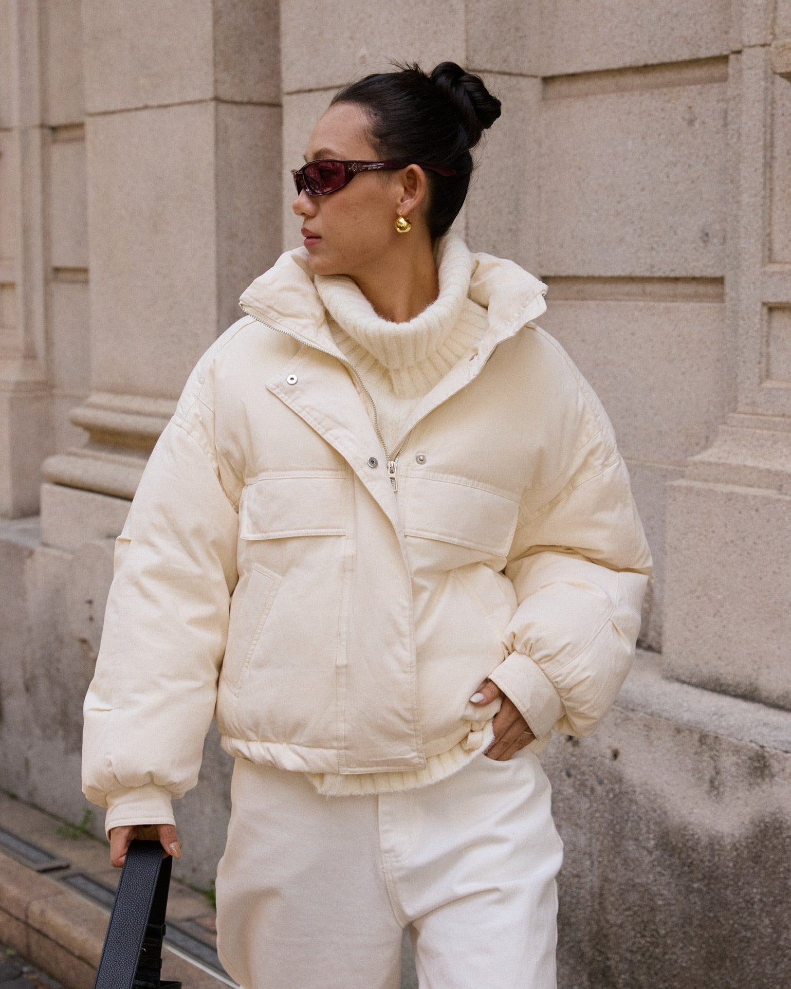 woman wearing a white puffer jacket and pants standing against a stone wall.