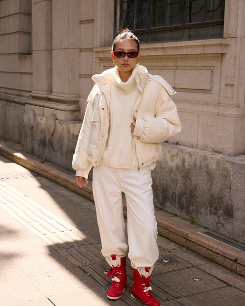 woman wearing a white outfit with red shoes standing on a sidewalk.