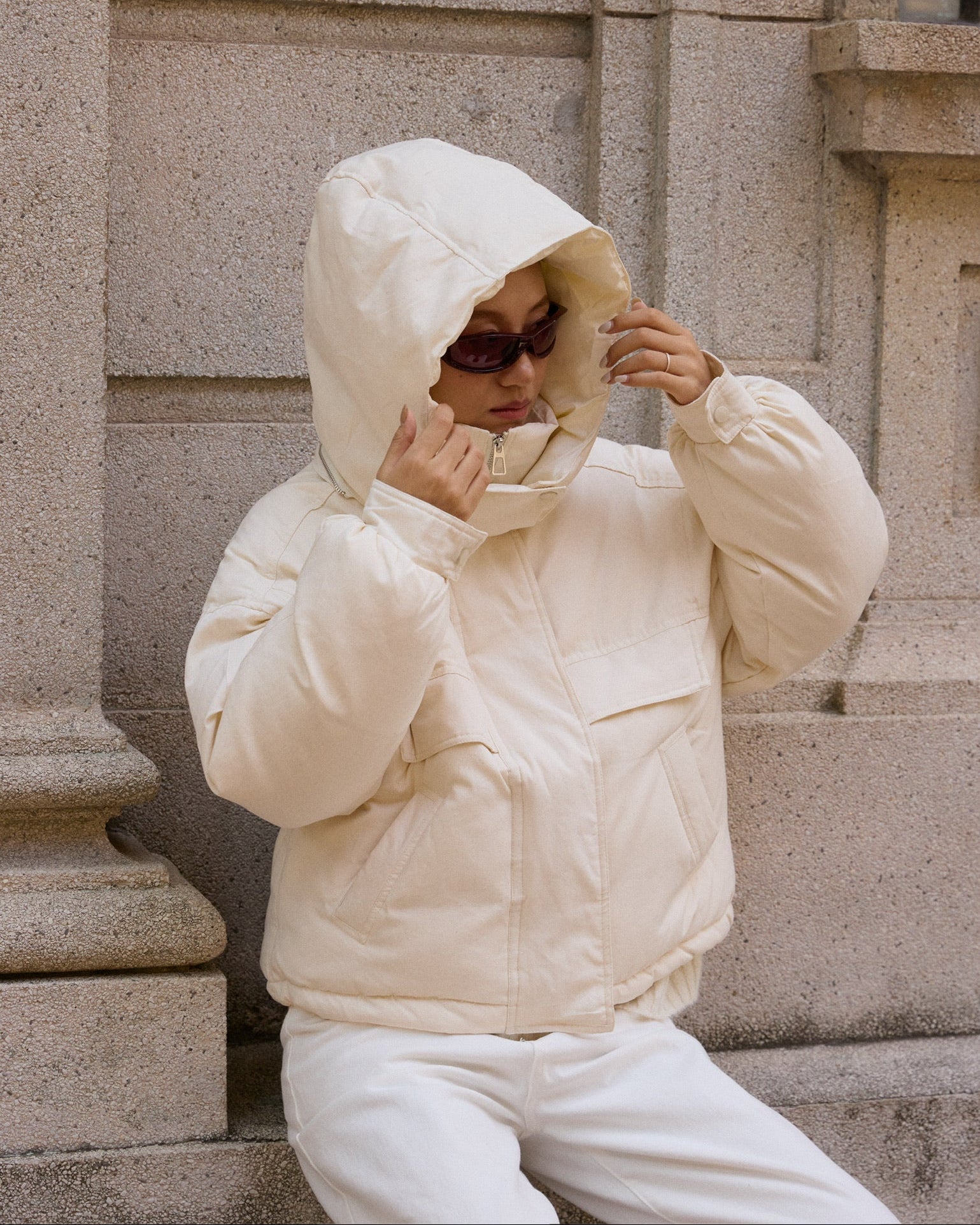 woman wearing a white puffer jacket sitting on stone steps.