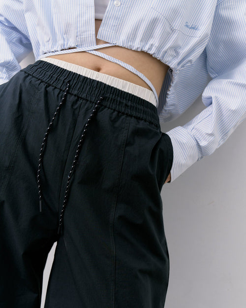 woman wearing a light blue striped shirt and black pants on a plain background