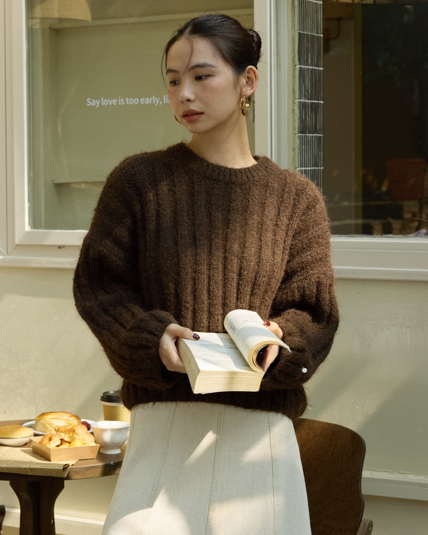 Woman in a brown sweater holding a book in an indoor setting