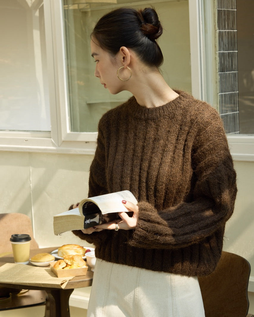 Woman in a brown sweater reading a book in a cozy indoor setting