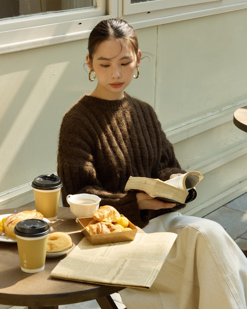 Woman reading a book with pastries and coffee on a wooden table outdoors.