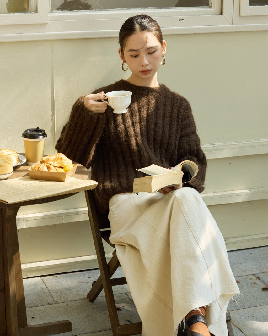 Woman sitting at an outdoor cafe, holding a cup and a book.