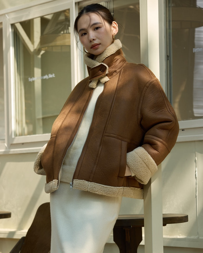 womanwearing a brown jacket with white fur trim sitting on a bench.