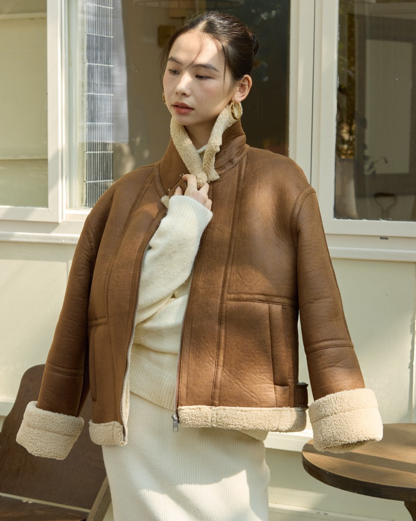Woman wearing a brown jacket with cream trim sitting outdoors.