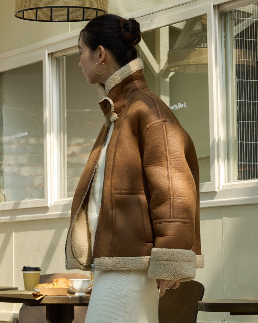 woman wearing a brown leather jacket with fur trim sitting at a table outdoors.