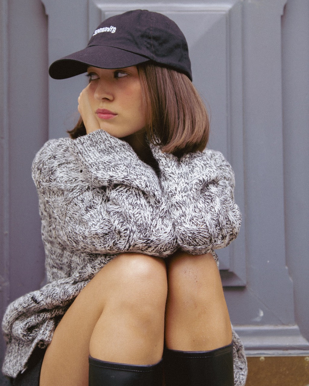 woman wearing a textured sweater and black cap against a gray wall.