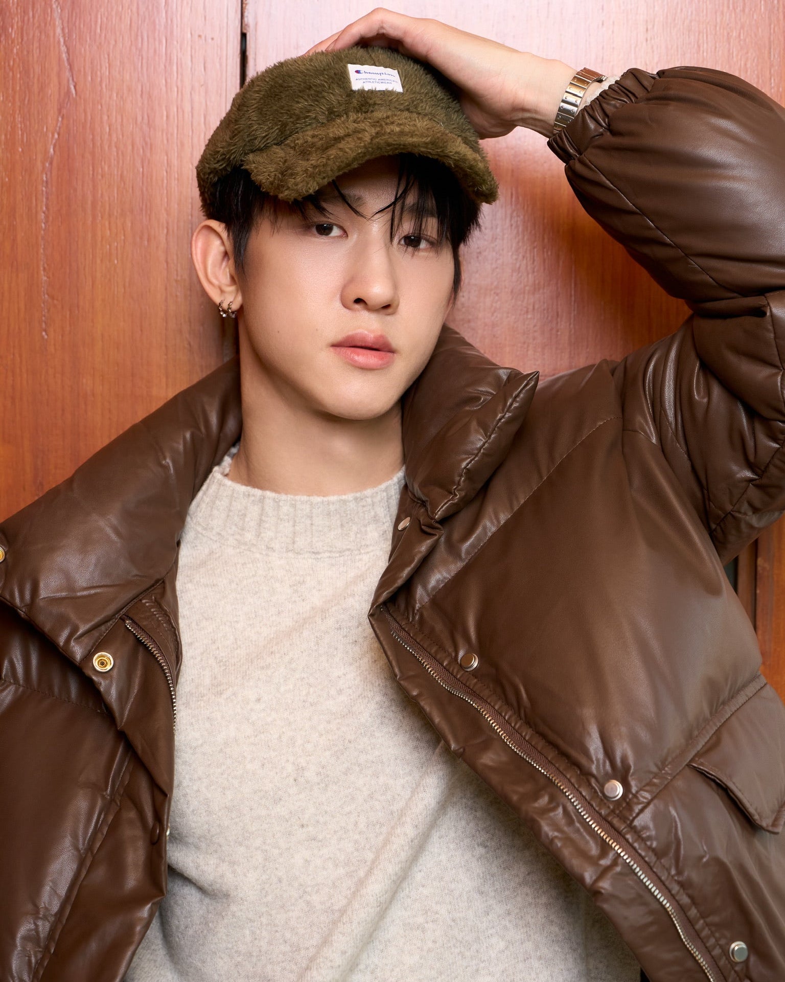 man wearing a brown jacket and cap against a wooden background