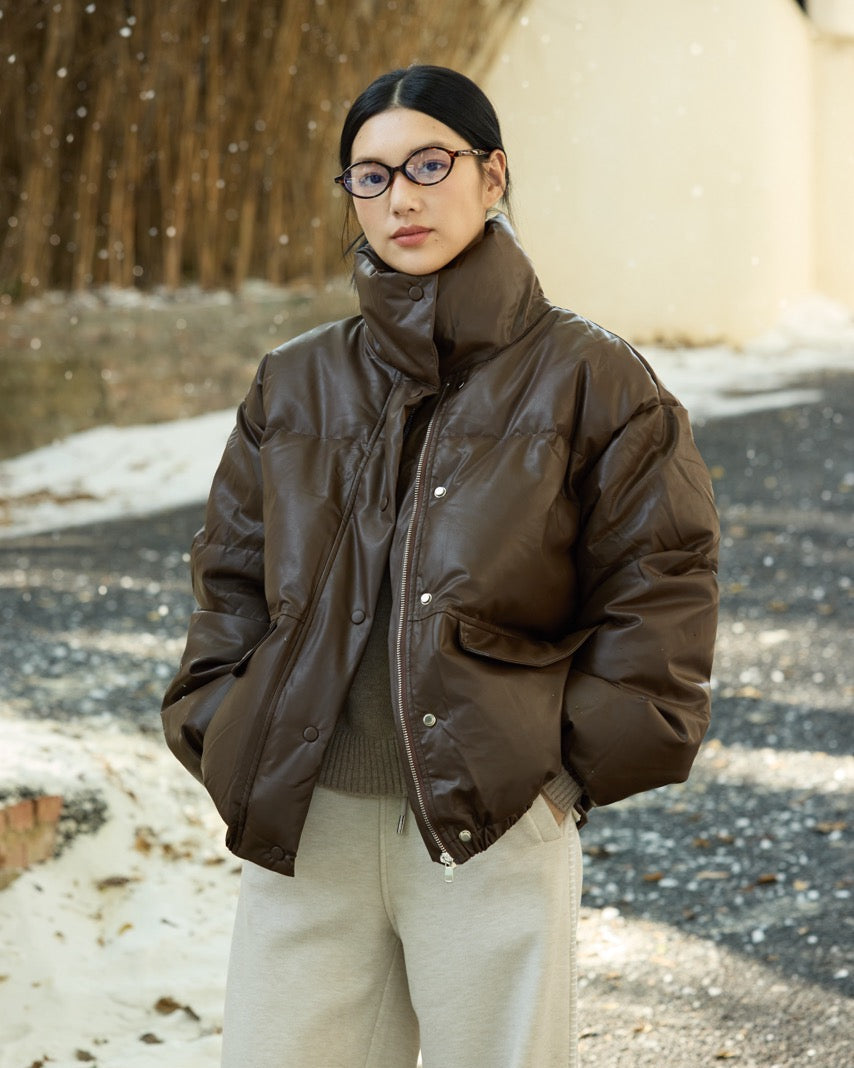 woman wearing a brown puffer jacket and glasses standing outdoors on a snowy day.