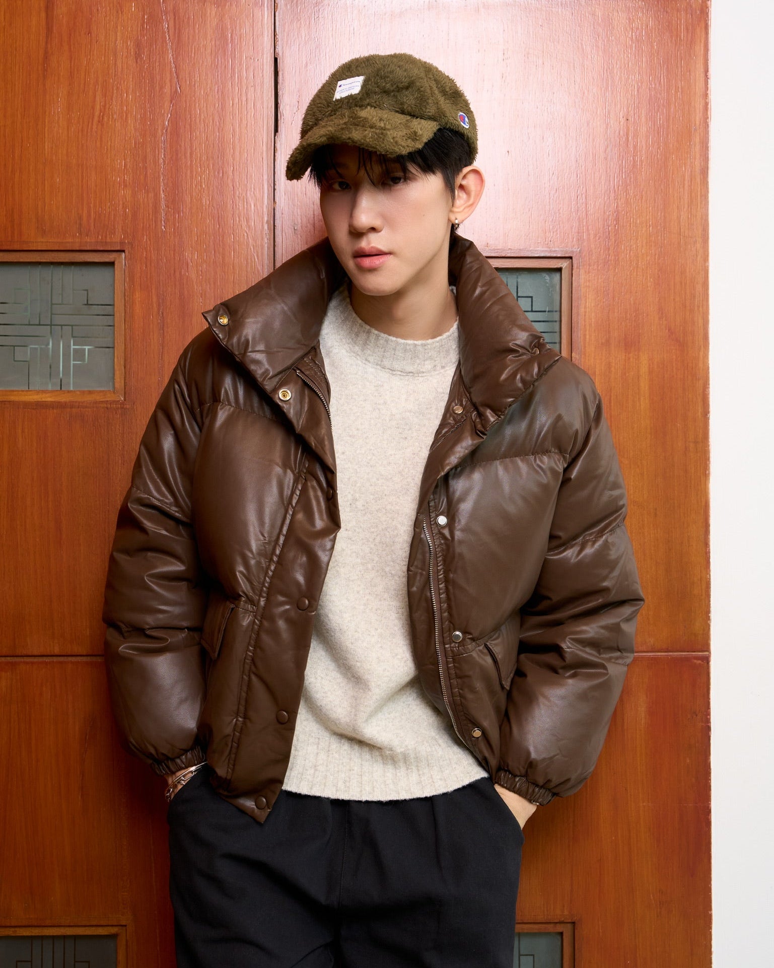 man wearing a brown leather jacket and cap against a wooden door.