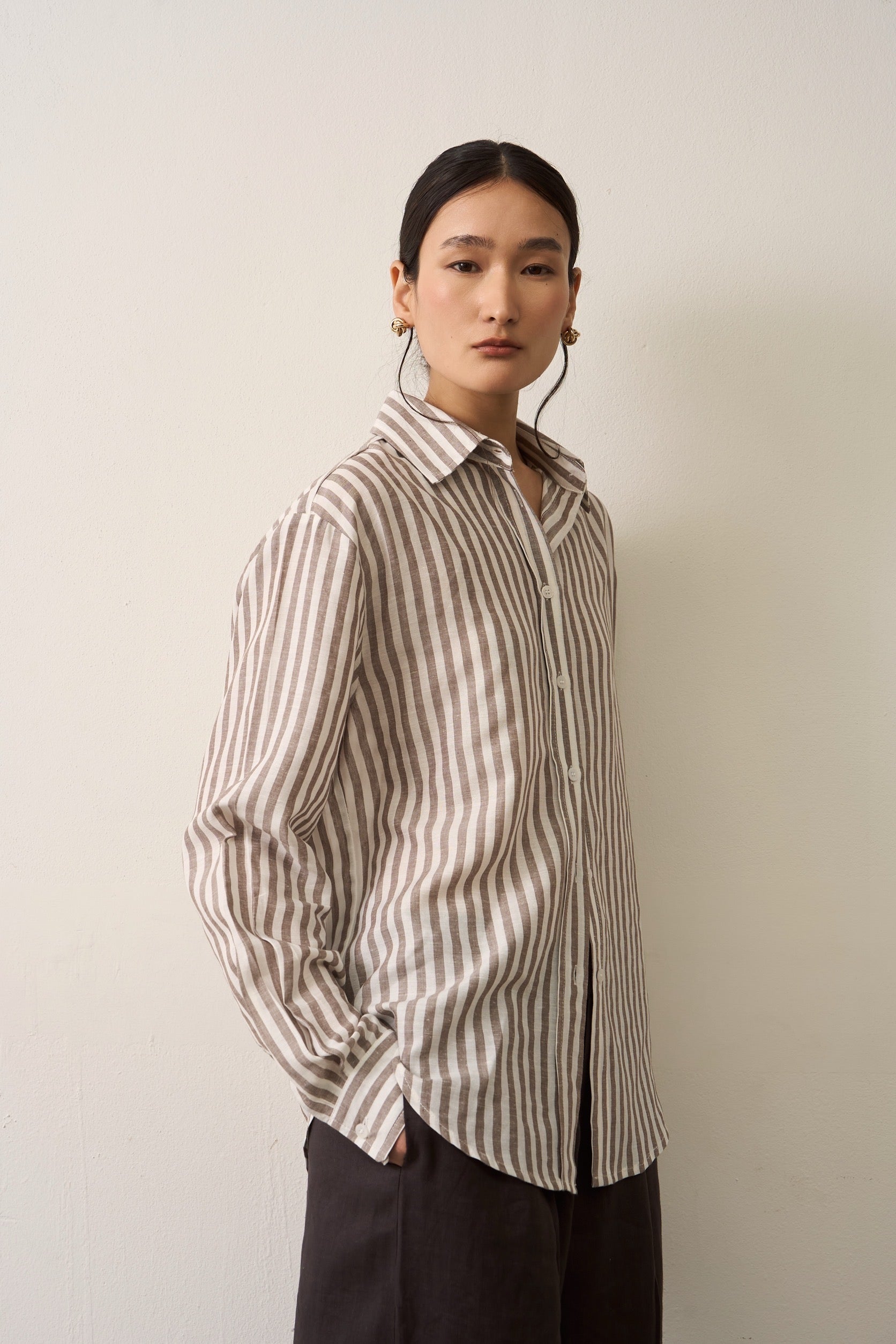 Close up of a woman wearing a brown striped linen shirt against a plain background