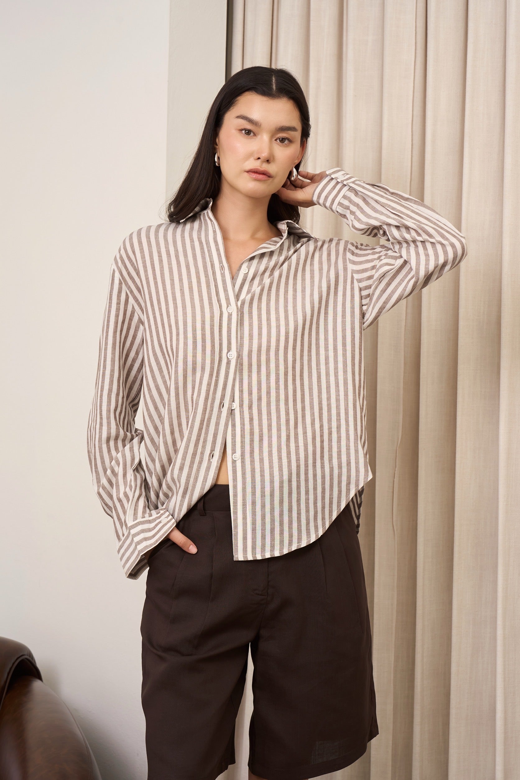 Woman wearing a brown striped shirt and brown burmuda shorts against a neutral background