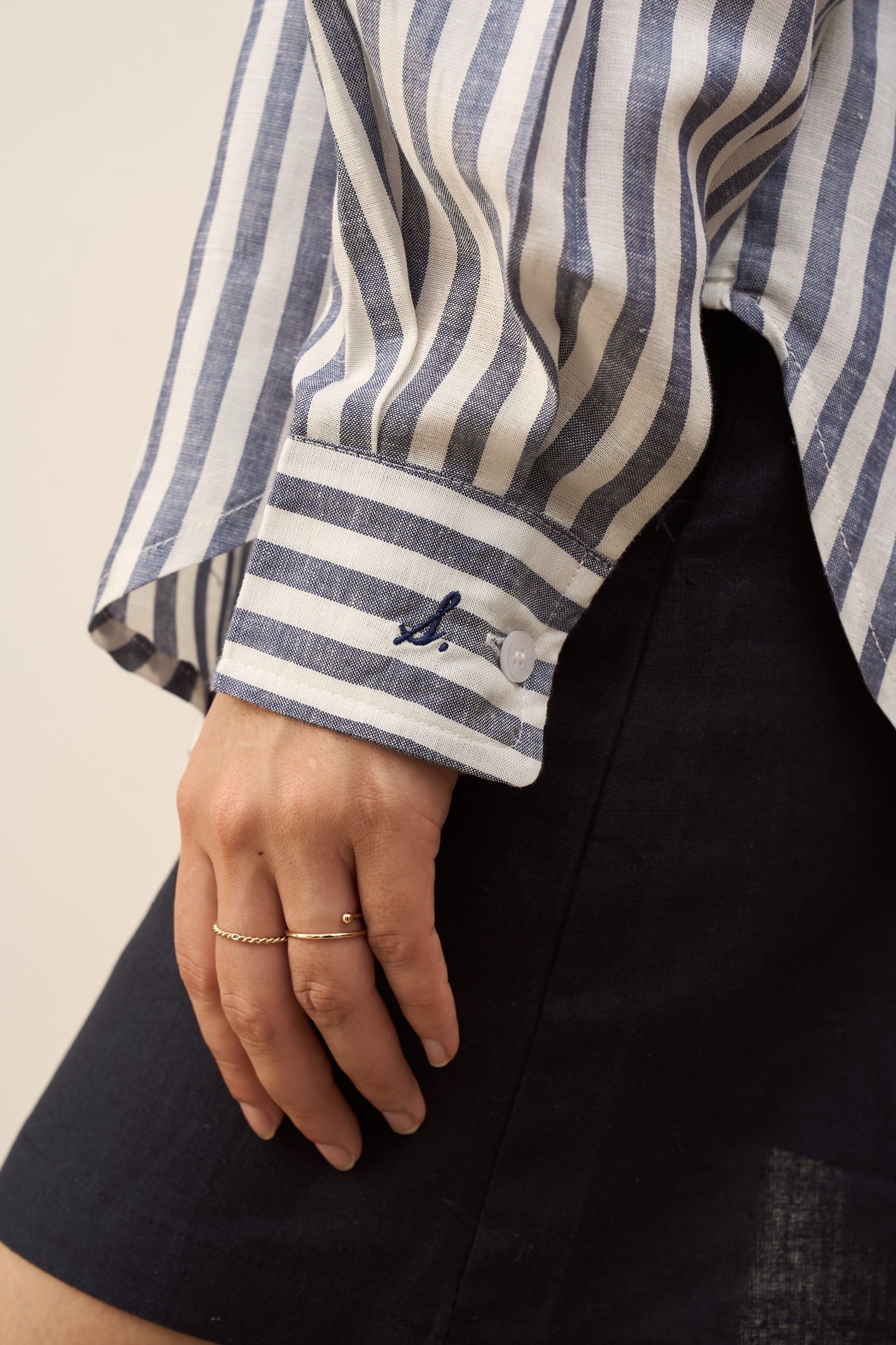Close-up of a woman wearing a navy striped linen shirt with signature embroidered at cuff.