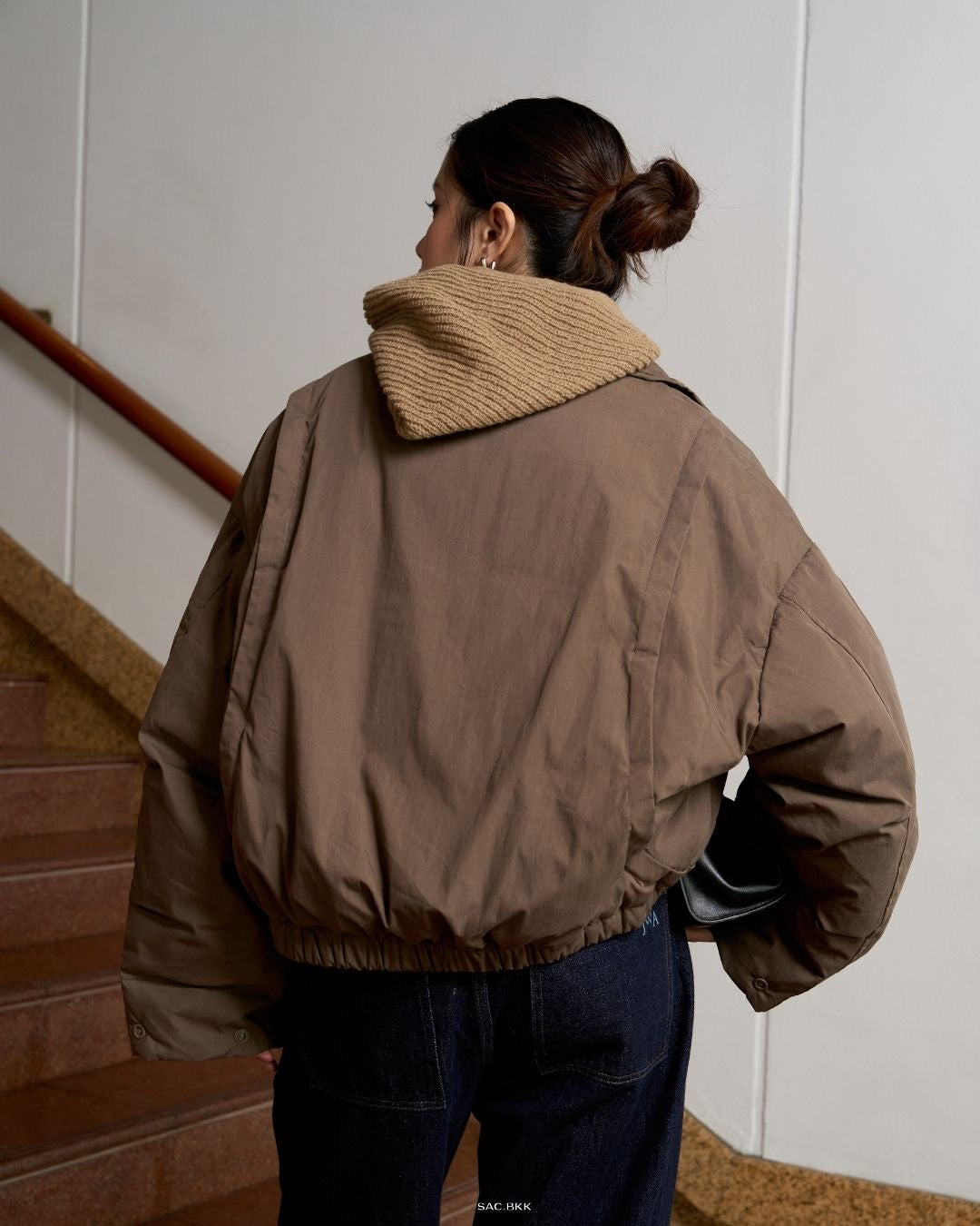 woman wearing a brown jacket with a textured collar, standing on a staircase.
