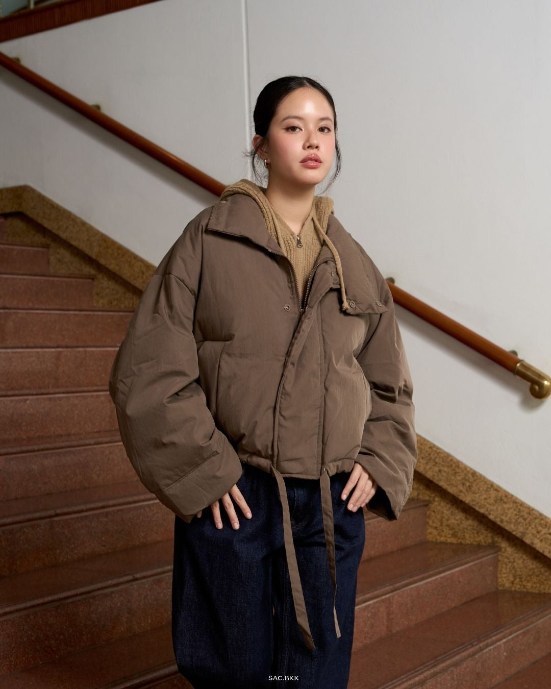 woman wearing a brown puffer jacket standing on a staircase.