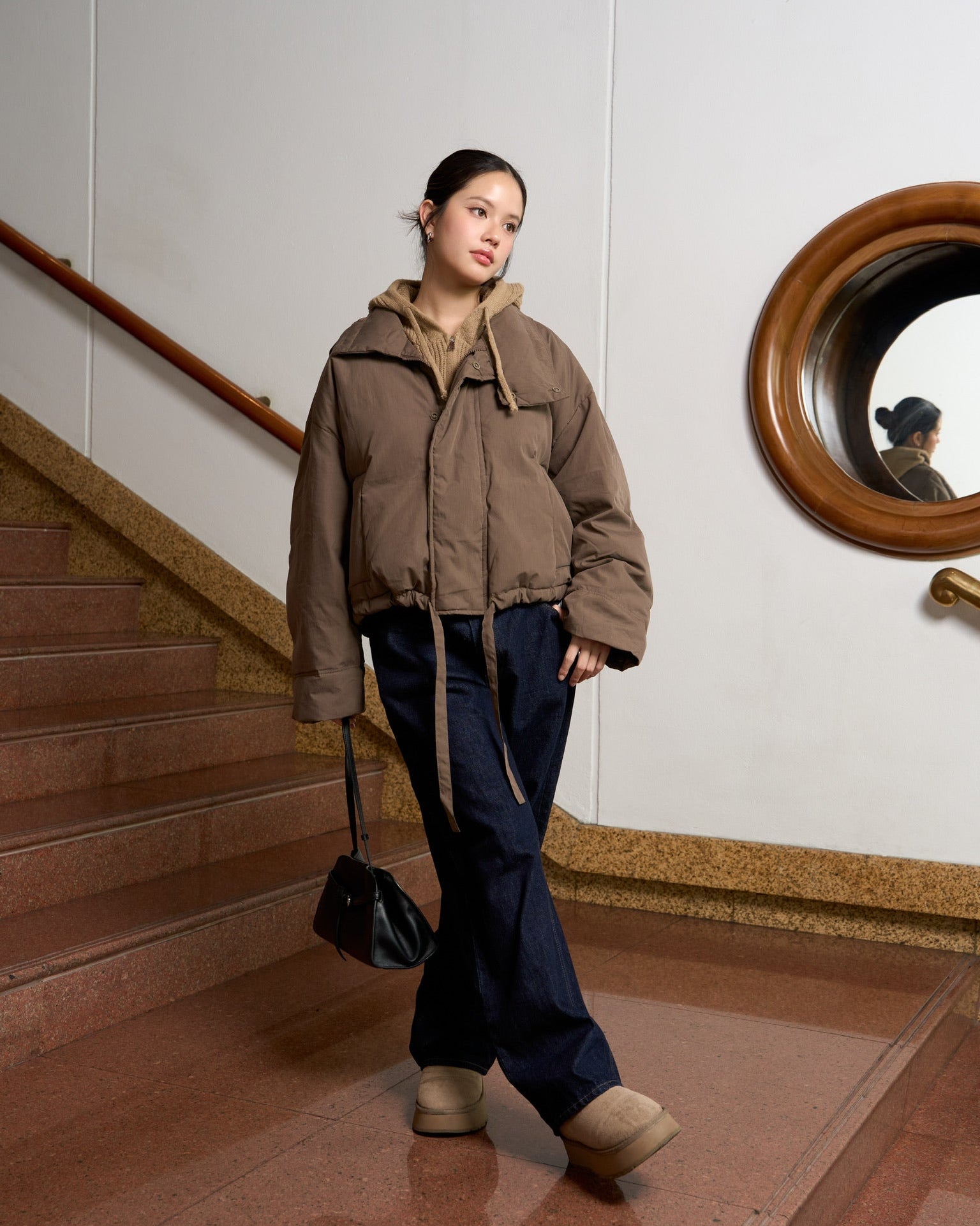 Woman in a brown jacket and dark pants walking down a staircase.