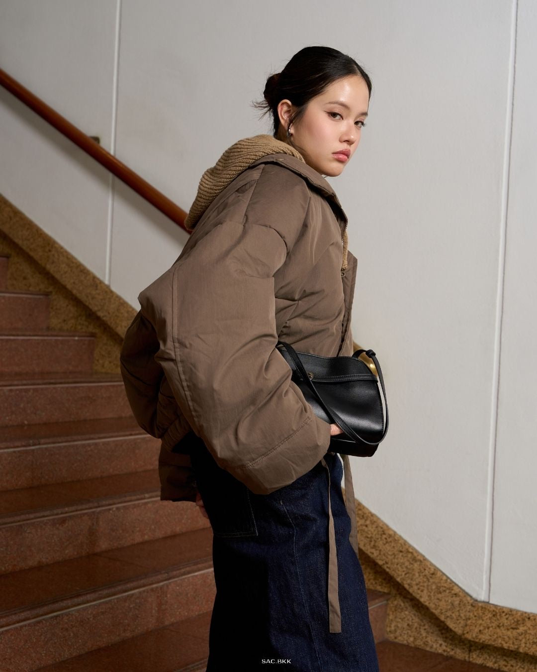 wearing a brown coat and holding a black bag on a staircase.