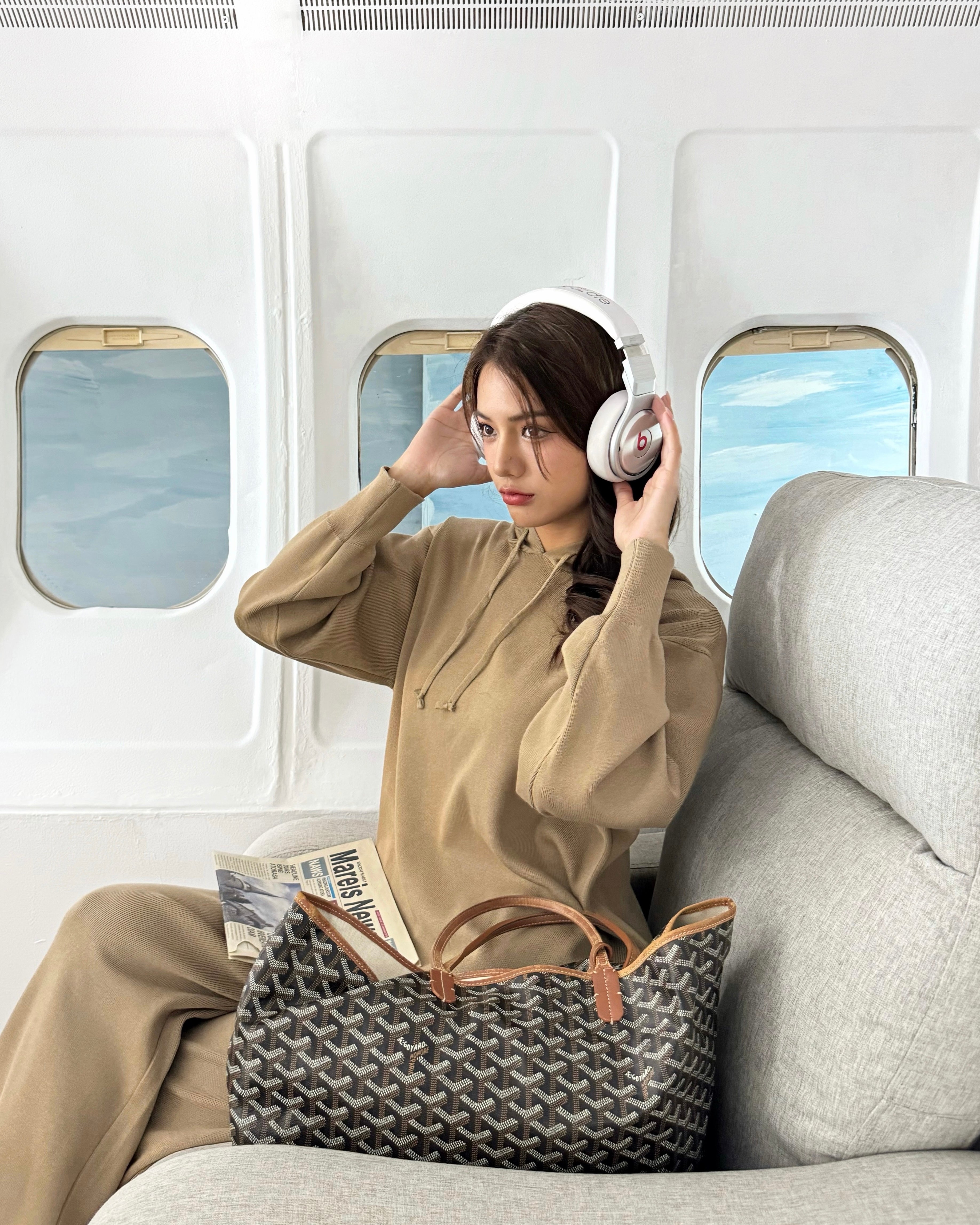 Woman sitting on an airplane with headphones on, holding a woven bag.