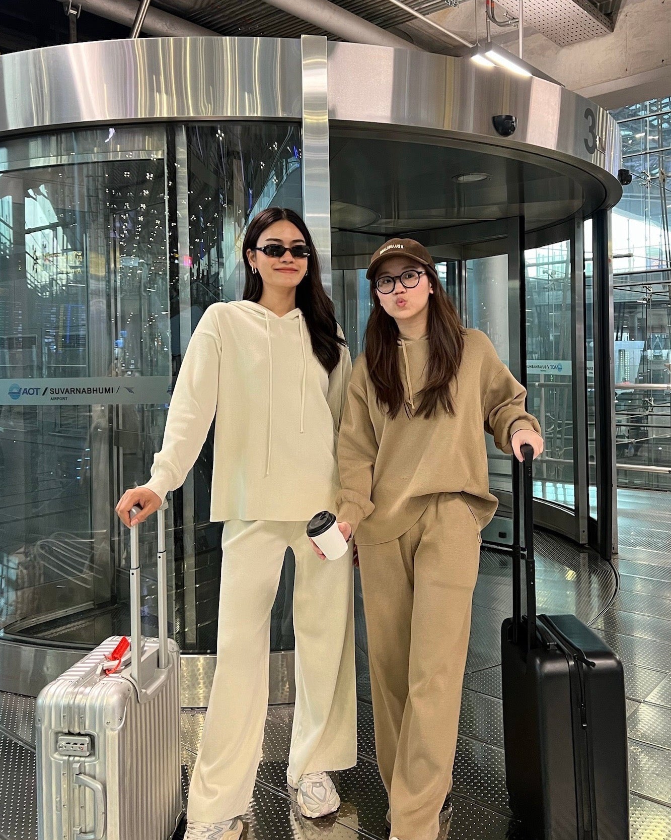Two women in matching outfits with suitcases at an airport.