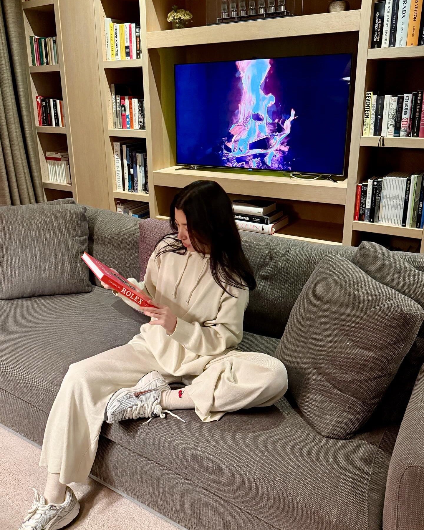Person sitting on a couch reading a book with a TV in the background displaying colorful graphics.
