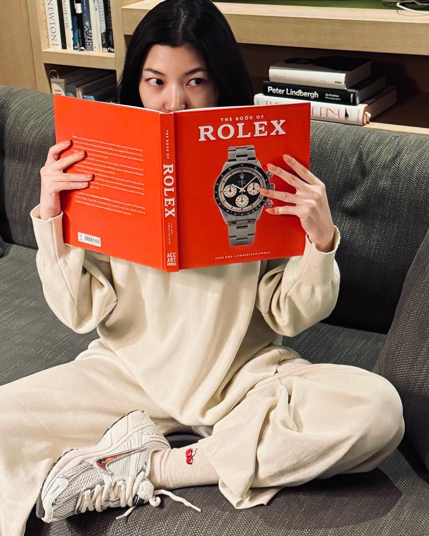 woman reading a book about Rolex watches on a couch.