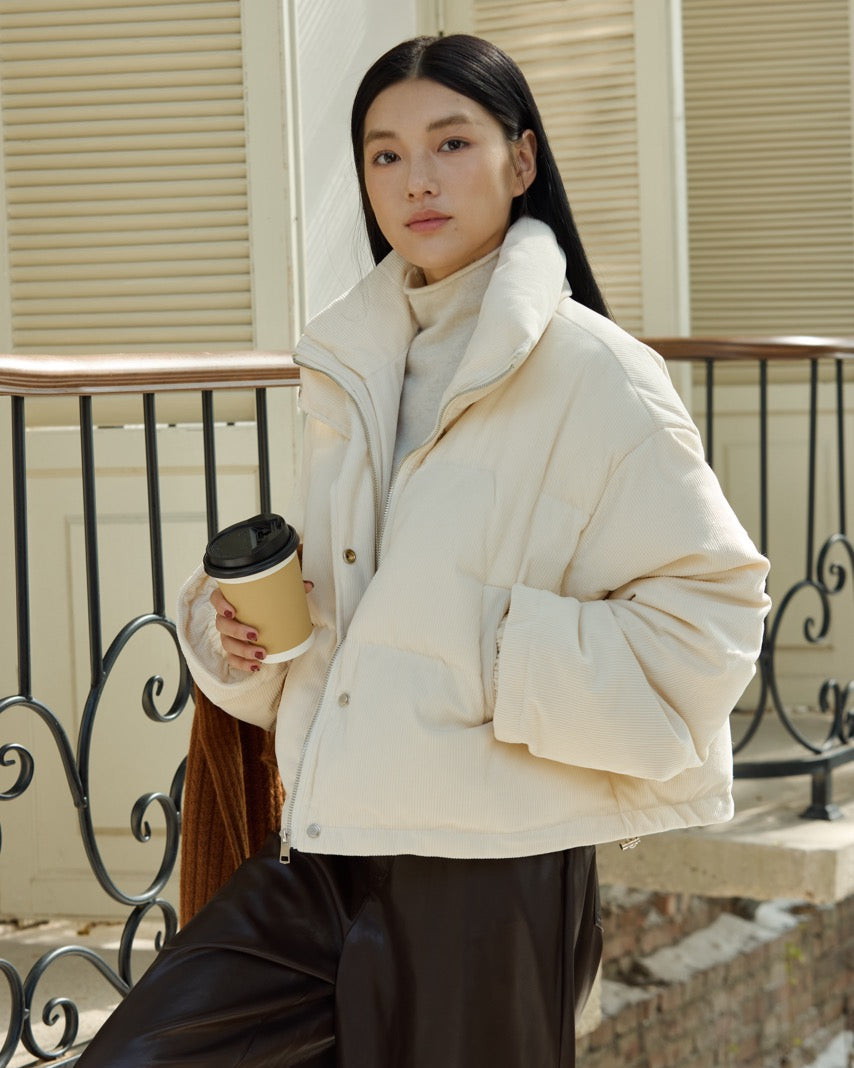 Woman in a white coat holding a coffee cup on a balcony