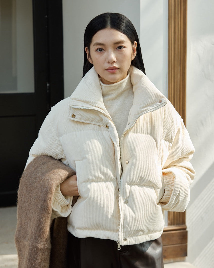 Woman wearing a cream puffer jacket and brown coat indoors.