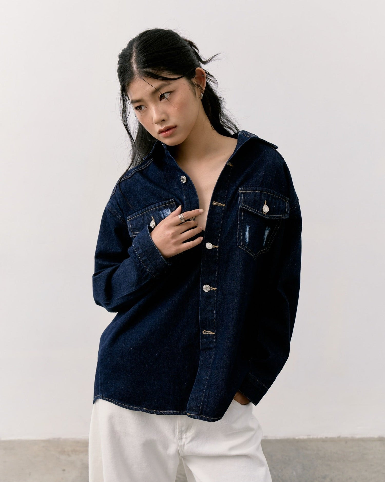 woman wearing a dark denim jacket and white pants against a plain background