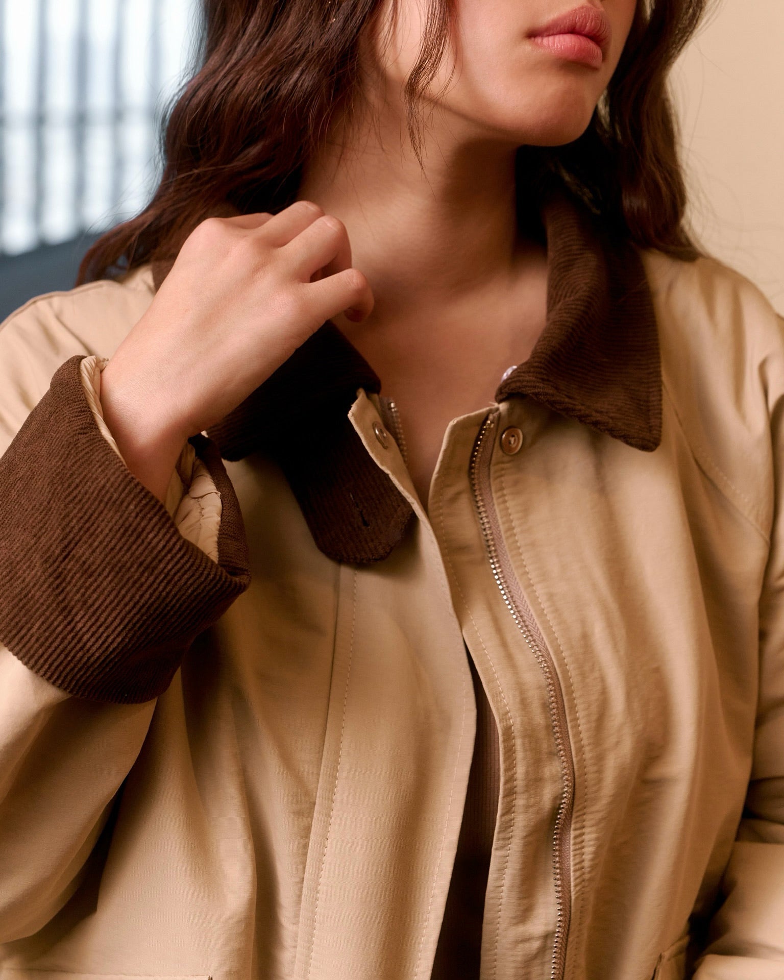Close-up of a person wearing a beige jacket with brown cuffs and collar.