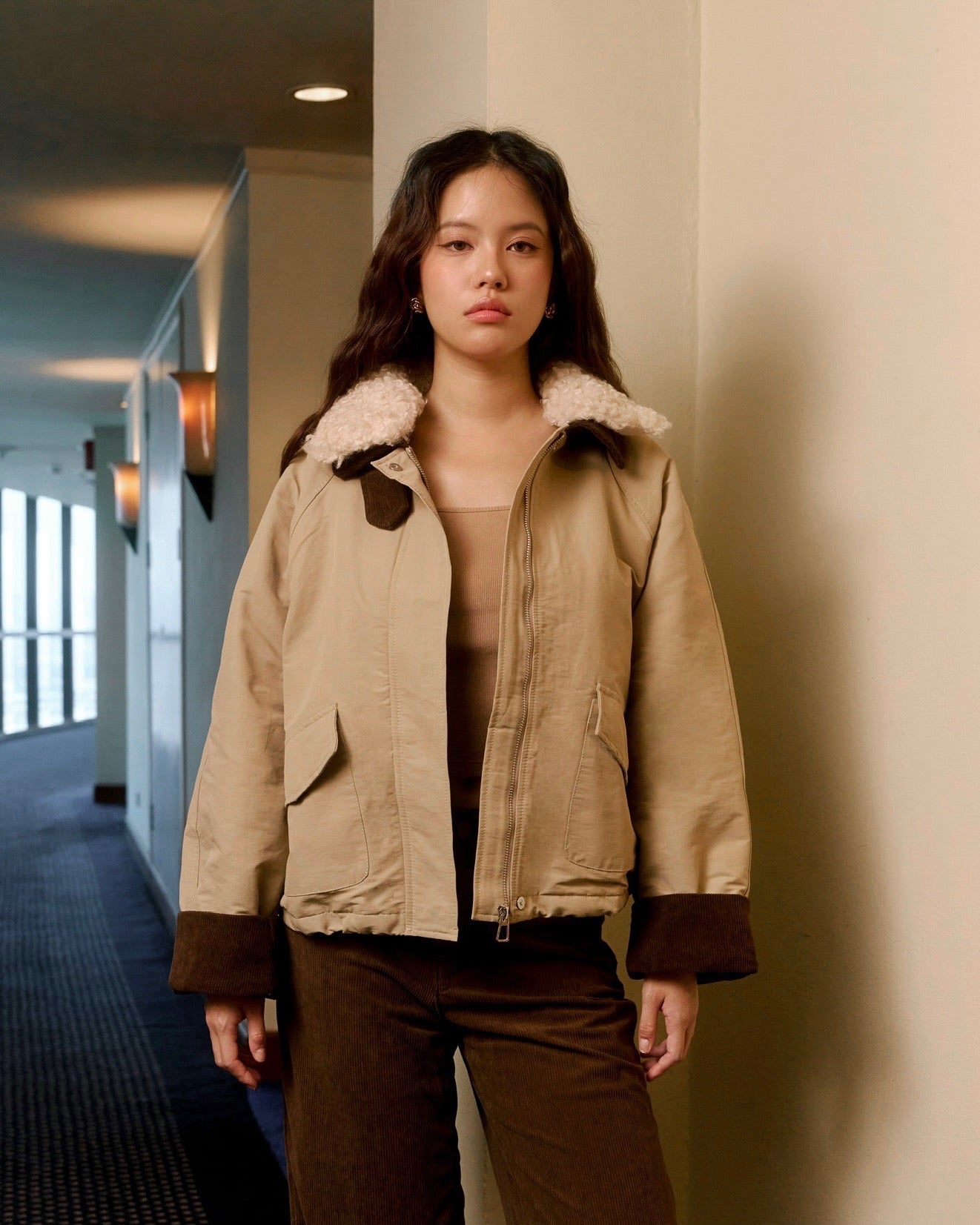 Woman wearing a beige jacket with fur-lined hood in an indoor setting