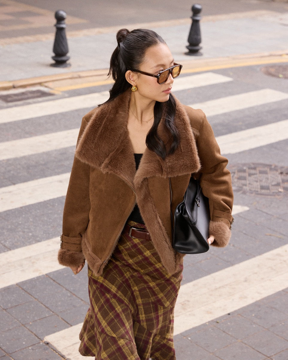 Woman wearing a brown coat and plaid skirt on a street.