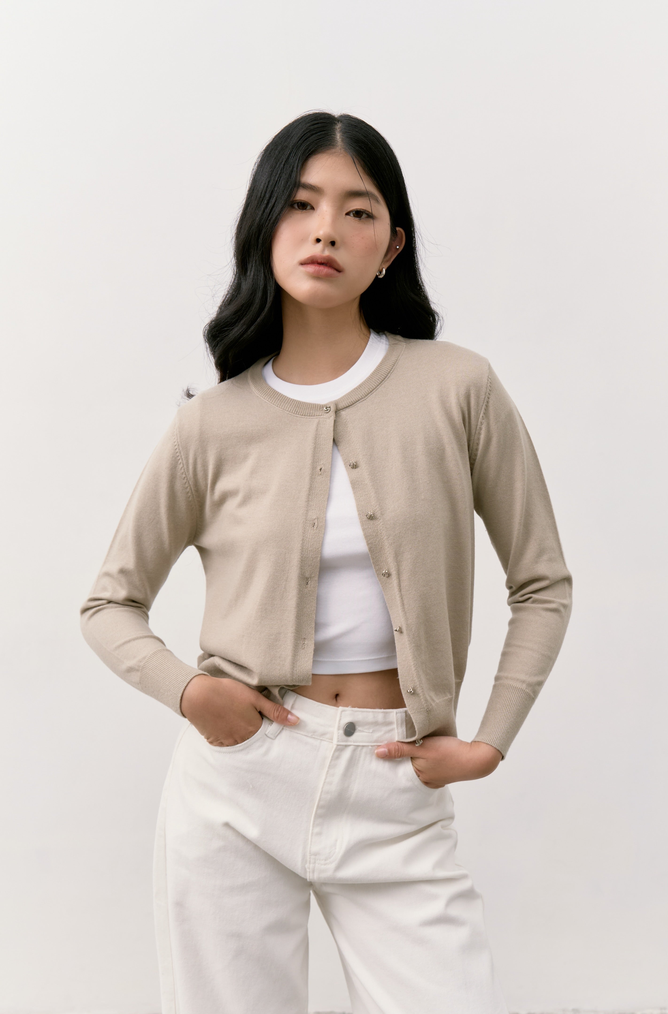 Woman wearing a beige Double S Cardigan, white t-shirt, and white pants against a plain background.