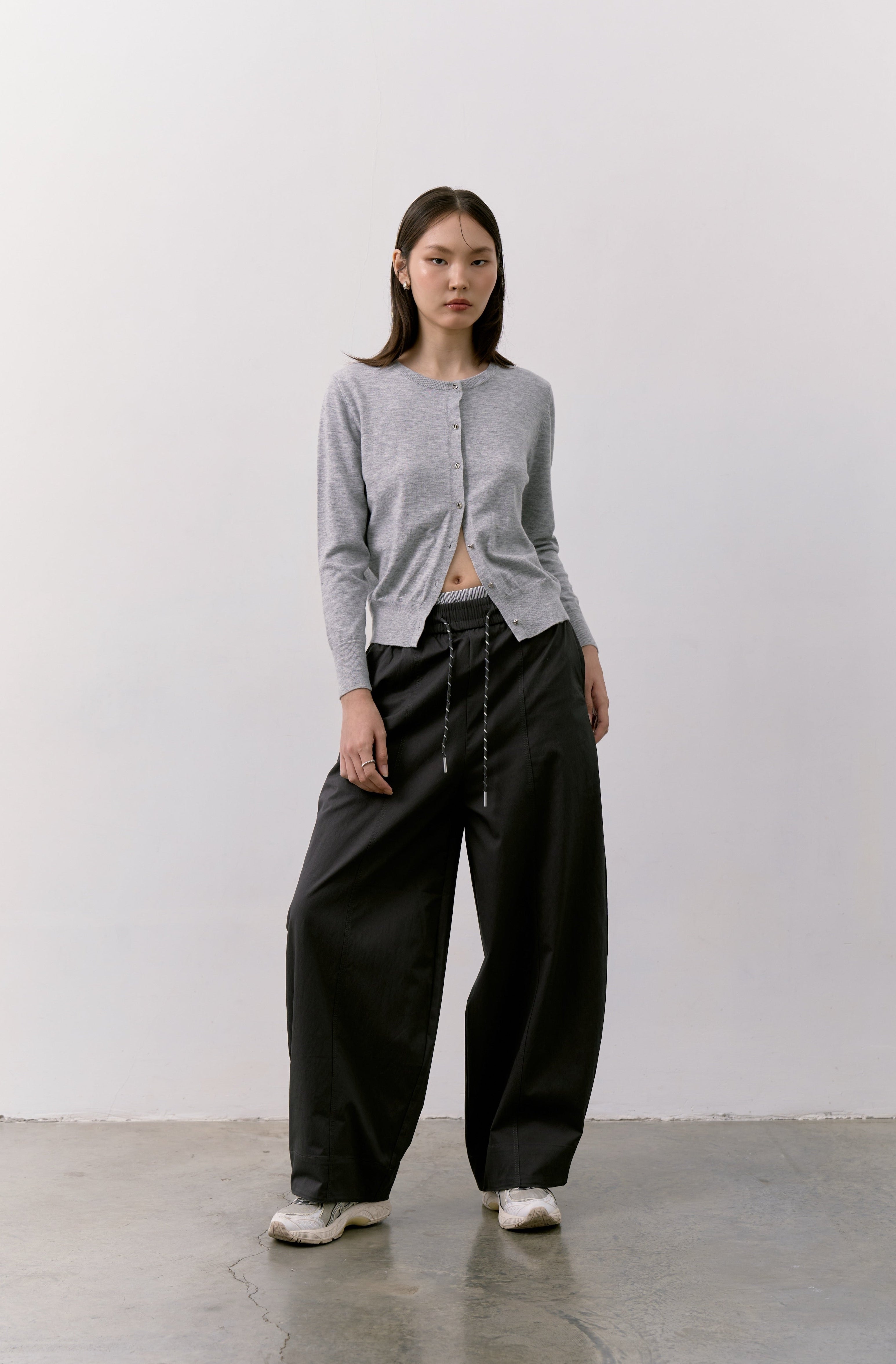 Woman wearing a gray Double S Cardigan ardigan and black barrel pants against a white background.