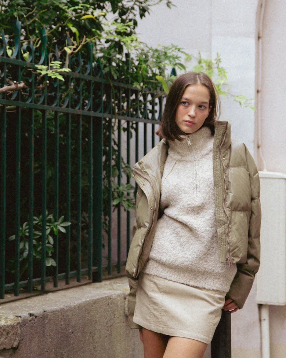 Woman wearing a beige puffer jacket over a cream dress in an outdoor setting.