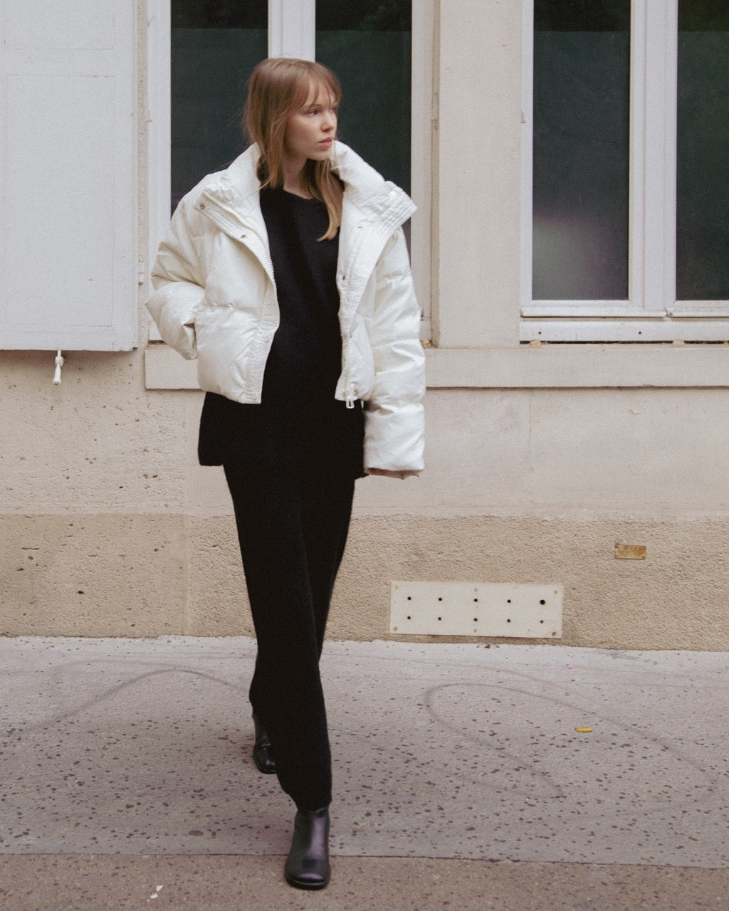 woman wearing a white puffer jacket over a black outfit standing on a sidewalk.