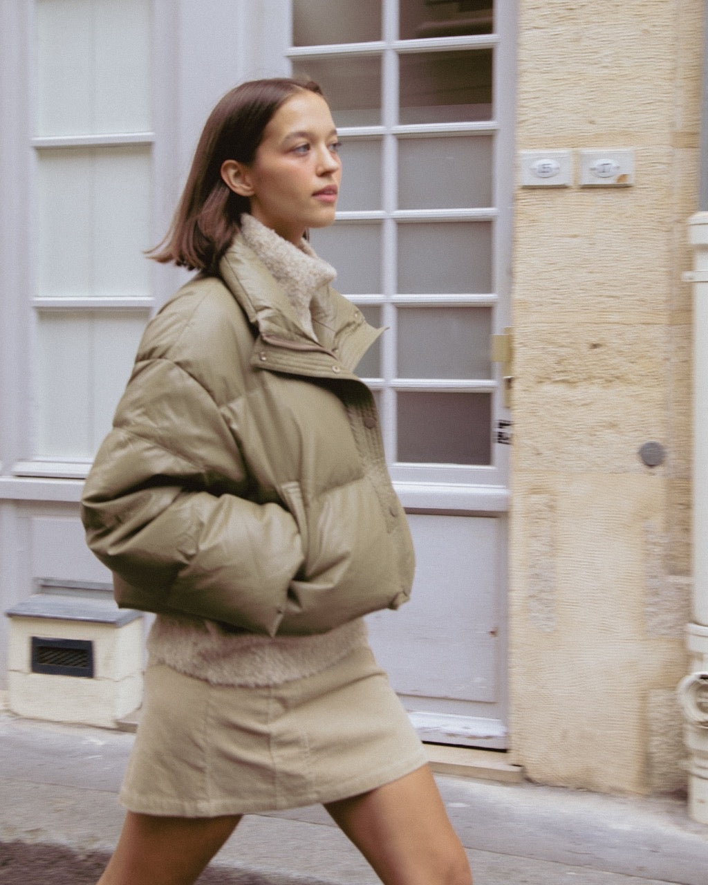 Woman wearing a beige puffer jacket and skirt walking on a street.