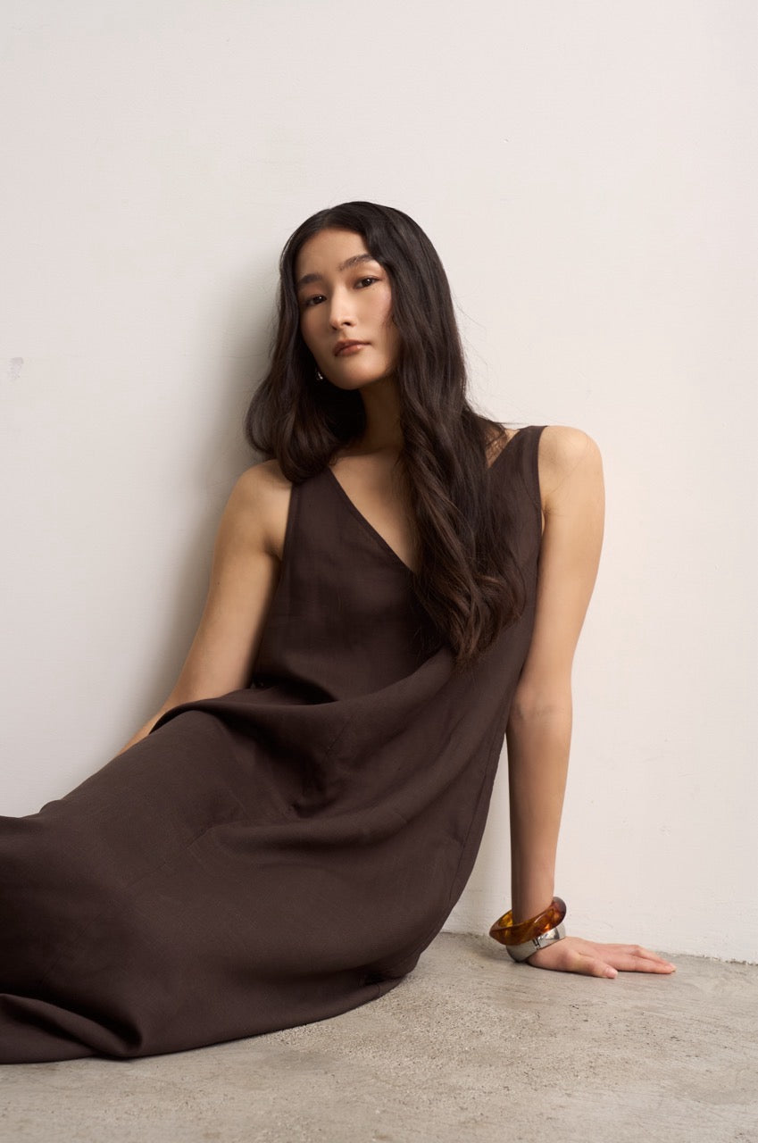 Woman wearing a sleeveless brown linen dress sitting against a plain background