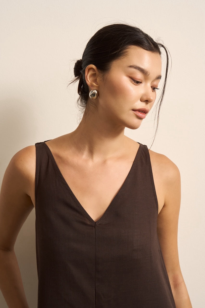 Close up of a woman wearing a brown sleeveless linen dress against a beige background