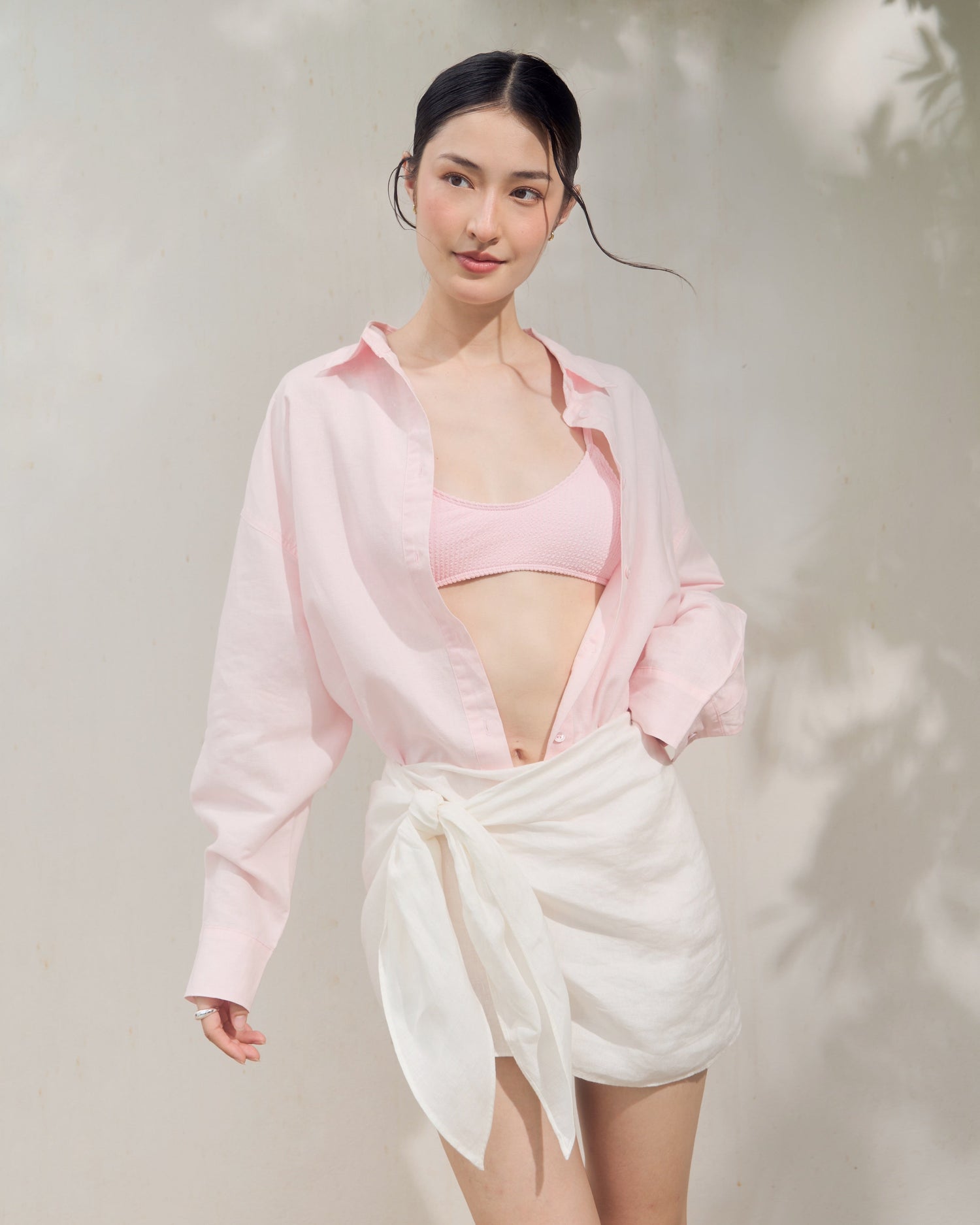 Woman wearing a pink top and white skirt against a light background