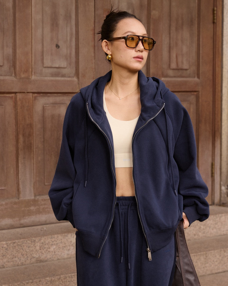 Woman wearing a navy blue tracksuit with sunglasses in front of a wooden door.