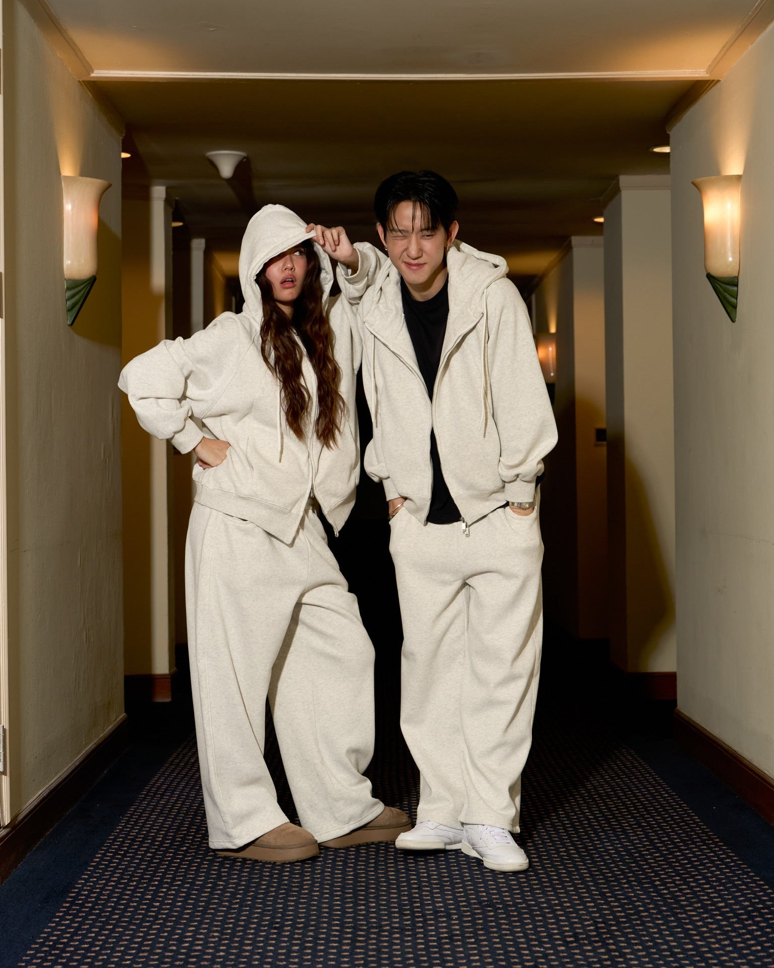 Two people in matching white outfits standing in a hallway.