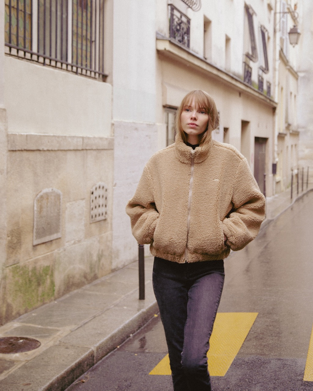 woman wearing a beige jacket walking on a city street.