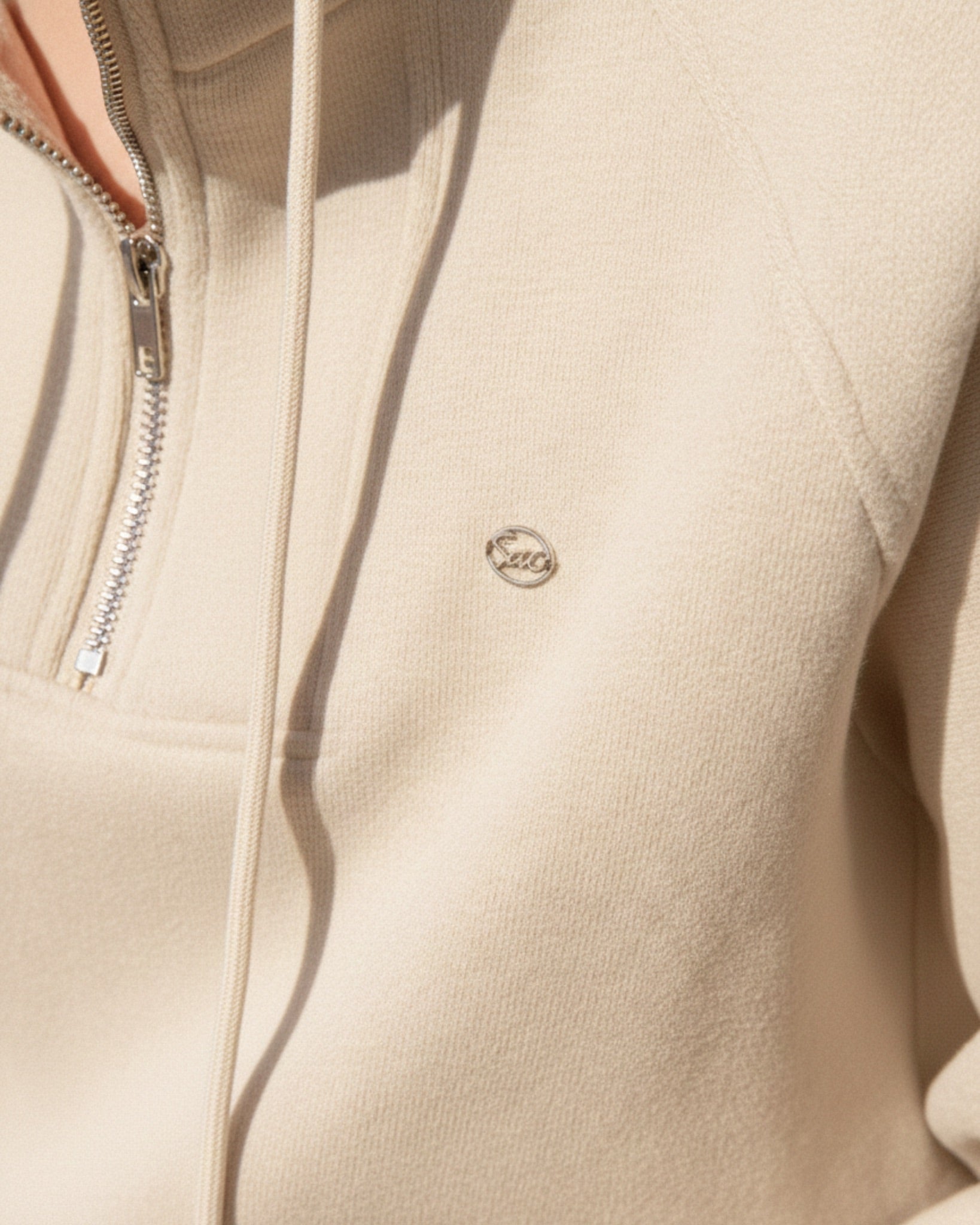 Close-up of a beige jacket with a zipper and a brand logo on the chest.